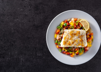 Grilled cod with vegetables in plate on black stone background