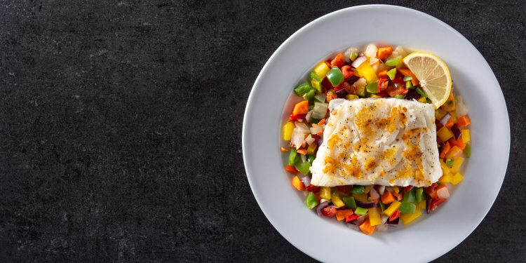Grilled cod with vegetables in plate on black stone background