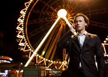 Portrait of young successful businessman in suit speaking on phone over night amusement park.